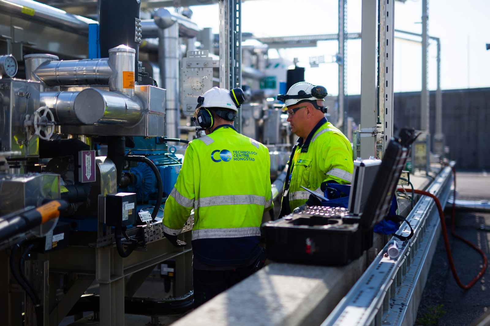 Arbeidere med arbeidstøy og hjelm ute på en fabrikk. Foto.