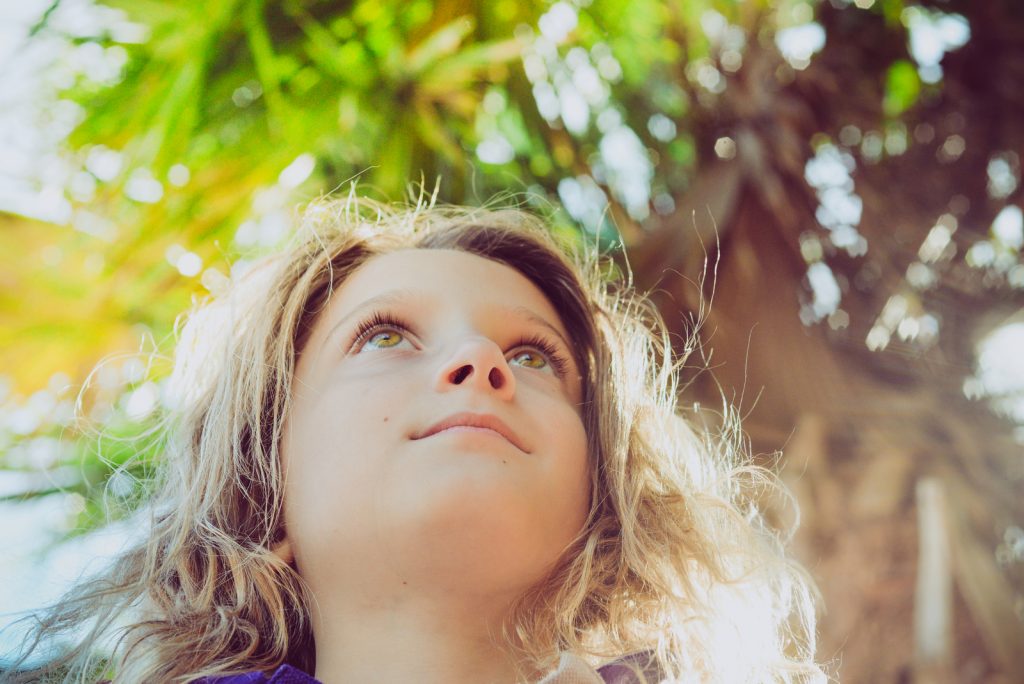 Sweet little girl in a outdoor portrait in a tropical sunny location. Her eyes look up to the 